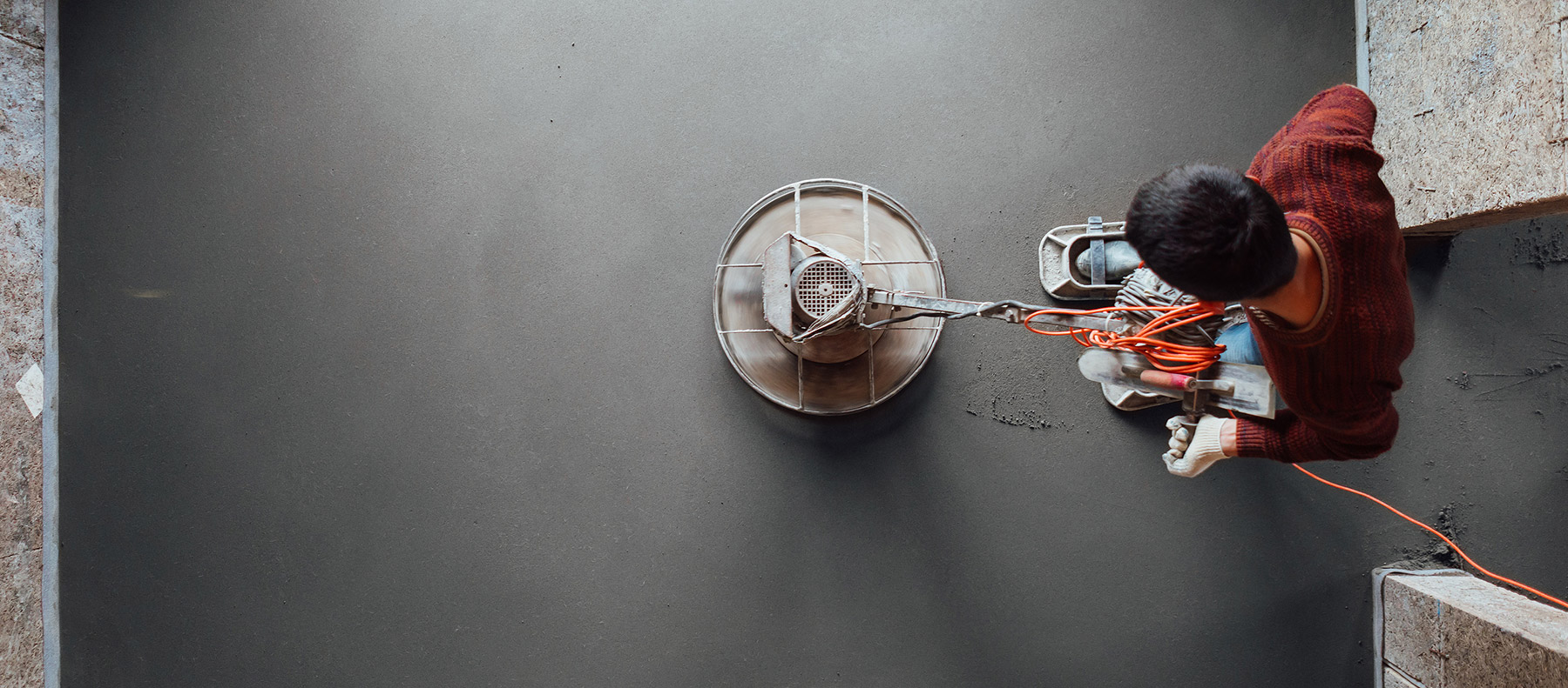 Worker using a rotary buffing machine to level and texture fresh concrete